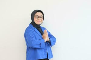 beautiful young Asian Muslim woman, wearing glasses and blue blazer with namaste gesture while smiling photo