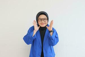 beautiful young Asian Muslim woman, wearing glasses and blue blazer with smiling open palms photo