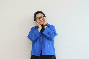 Beautiful young Asian woman in glasses, hijab and wearing blue blazer posing with smiling face photo