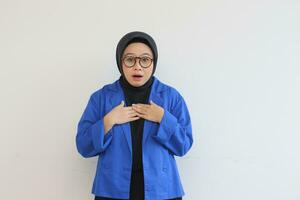 Beautiful young Asian Muslim woman in glasses and smiling putting both hands on chest and showing affection gesture photo