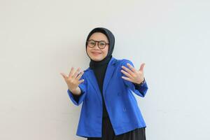 beautiful young Asian Muslim woman, wearing glasses and blue blazer with smiling open palms photo