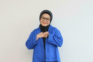 Beautiful young Asian Muslim woman in glasses and smiling putting both hands on chest and showing affection gesture photo