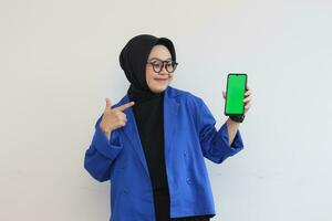 smiling beautiful asian women in blue blazer and hijab showing green screen mobile phone photo