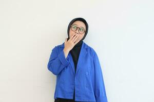 beautiful young Asian Muslim woman, wearing glasses and blue blazer with shocked expression while covering mouth photo