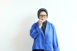 Beautiful young Asian Muslim woman, wearing glasses and blue blazer with disgusted face expression photo