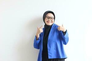 joven hermosa asiático musulmán mujer, vistiendo lentes y azul chaqueta de sport con contento sonriente cara expresión foto