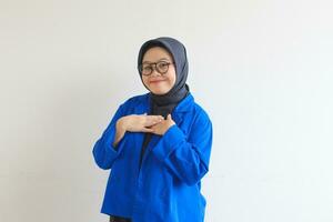 Beautiful young Asian Muslim woman in glasses and smiling putting both hands on chest and showing affection gesture photo