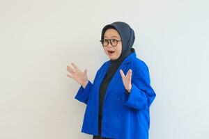 beautiful young Asian Muslim woman, wearing glasses and blue blazer with shocked expression photo