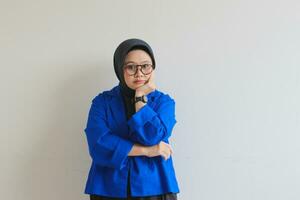 Beautiful young Asian Muslim woman, wearing a blue blazer looking at the camera with a straight face expression photo