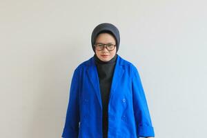joven hermosa asiático musulmán mujer, vistiendo lentes y azul chaqueta de sport con enojado facial expresión foto