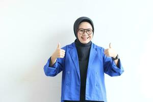 beautiful young Asian Muslim woman, wearing glasses and blue blazer with hand gesture of approval or OK photo