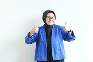 beautiful young Asian Muslim woman, wearing glasses and blue blazer with hand gesture of approval or OK photo