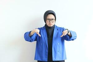 Beautiful young Asian Muslim woman, wearing glasses and blue blazer with hand and face gesturing downplaying something or disappointed photo