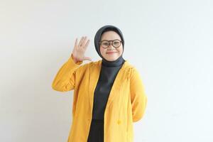 hermosa joven asiático musulmán mujer, vistiendo lentes y amarillo chaqueta de sport demostración palmas mientras sonriente aislado blanco antecedentes. publicidad concepto. foto