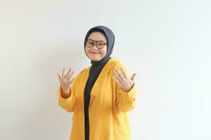 Young beautiful Asian Muslim woman, wearing glasses and yellow blazer with happy smiling face expression photo