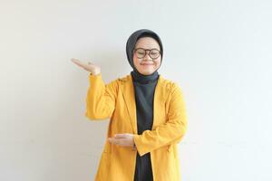 hermosa joven asiático musulmán mujer, vistiendo lentes y amarillo chaqueta de sport demostración palmas mientras sonriente foto