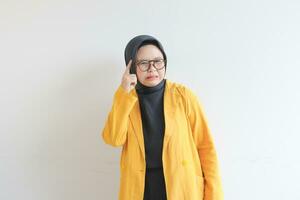 Beautiful young Asian Muslim woman, wearing glasses and yellow blazer is thinking photo
