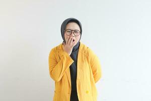 Beautiful young Asian Muslim woman, wearing glasses and yellow blazer yawning photo