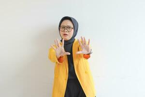 Beautiful young Asian Muslim woman, wearing glasses and yellow blazer with scared face expression photo