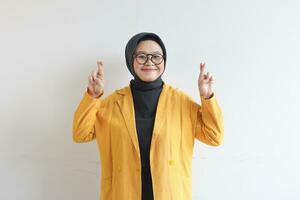 Young beautiful Asian Muslim woman, wearing glasses and yellow blazer with happy smiling face expression photo