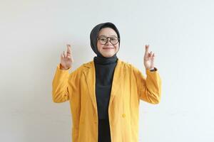 Young beautiful Asian Muslim woman, wearing glasses and yellow blazer with happy smiling face expression photo