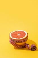 Fruit orange is wrapped with measuring tape on yellow background. photo