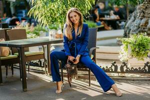 attractive woman dressed in blue elegant suit sitting in cafe in city street photo