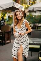 beautiful smiling woman dressed in white printed dress in street cafe photo