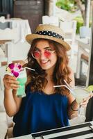 attractive young woman in blue dress and straw hat wearing pink sunglasses drinking cocktails photo