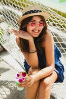 attractive young woman in blue dress and straw hat wearing pink sunglasses drinking cocktails photo