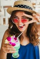 attractive young woman in blue dress and straw hat wearing pink sunglasses drinking cocktails photo