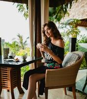 young stylish beautiful woman sitting at tropical resort cafe photo