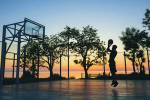negro hombre haciendo Deportes, jugando baloncesto en amanecer, saltando silueta foto