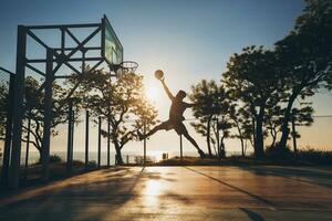 black man doing sports, playing basketball on sunrise, jumping silhouette photo