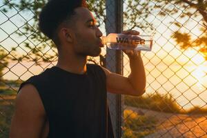 negro hombre haciendo Deportes en mañana, Bebiendo agua en baloncesto Corte en amanecer foto