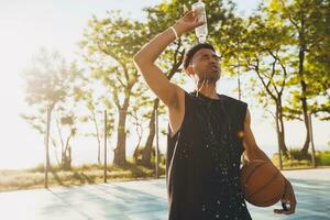 close-up portrait of young black man doing sports in morning, drinking water on basketball court photo