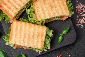 Delicious crispy sandwich with toast, salmon, avocado, tomatoes, salt, spices and herbs photo