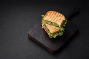 Delicious crispy sandwich with toast, salmon, avocado, tomatoes, salt, spices and herbs photo