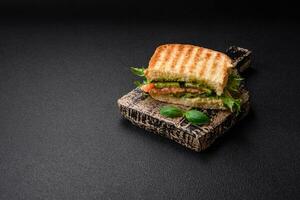 Delicious crispy sandwich with toast, salmon, avocado, tomatoes, salt, spices and herbs photo
