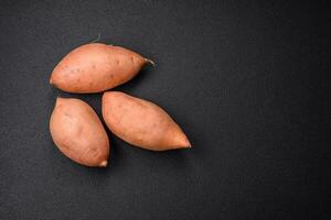 Fresh large pink sweet potato tubers with tomatoes and spices on a dark background photo