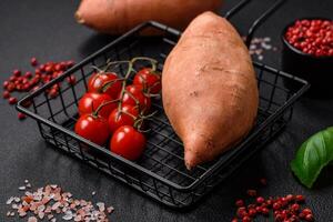 Fresh large pink sweet potato tubers with tomatoes and spices on a dark background photo