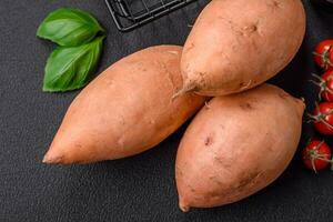 Fresh large pink sweet potato tubers with tomatoes and spices on a dark background photo