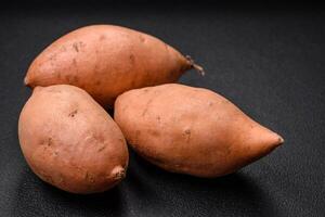 Fresh large pink sweet potato tubers with tomatoes and spices on a dark background photo