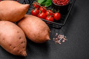 Fresh large pink sweet potato tubers with tomatoes and spices on a dark background photo