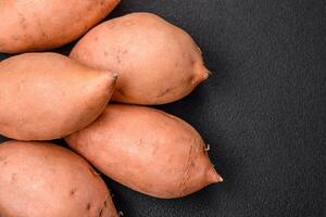 Fresh large pink sweet potato tubers with tomatoes and spices on a dark background photo