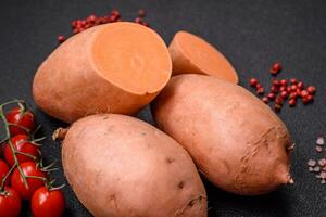 Fresh large pink sweet potato tubers with tomatoes and spices on a dark background photo