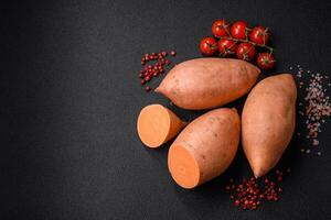 Fresh large pink sweet potato tubers with tomatoes and spices on a dark background photo