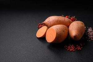 Fresco grande rosado dulce patata tubérculos con Tomates y especias en un oscuro antecedentes foto