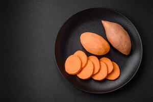 Fresh large pink sweet potato tubers with tomatoes and spices on a dark background photo