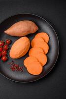 Fresh large pink sweet potato tubers with tomatoes and spices on a dark background photo